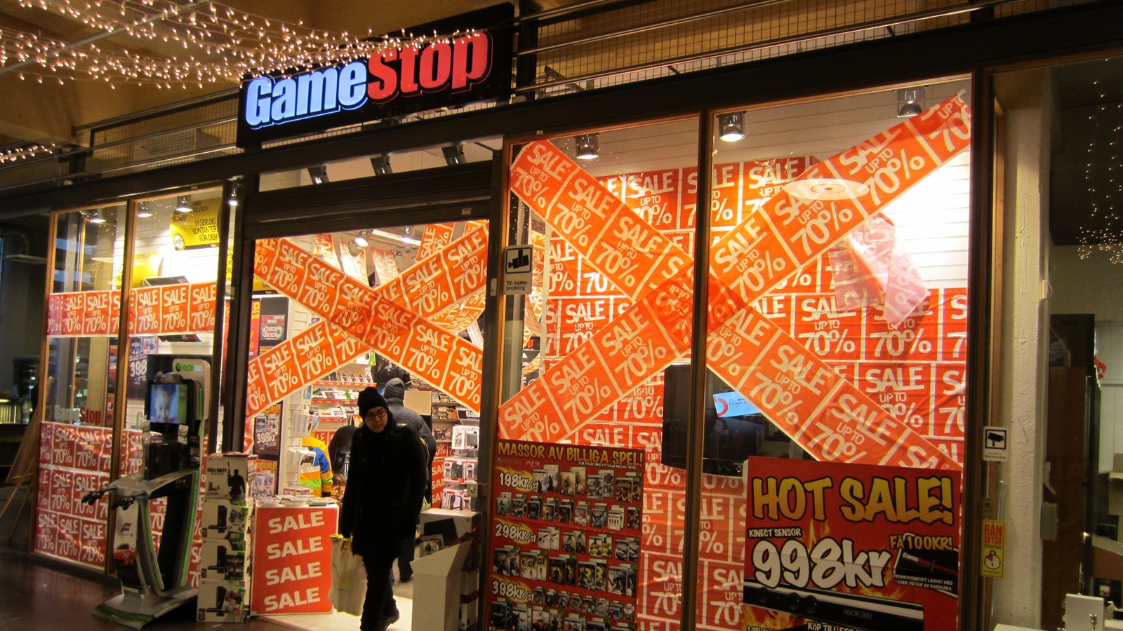 The storefront of a GameStop video game shop, its windows covered in sale posters